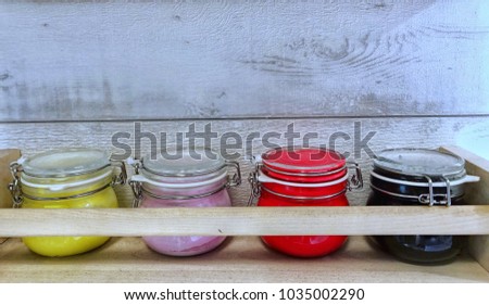 Colorful poder in glass jars on a wooden shelf.