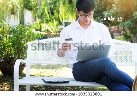 Young business man sitting on the park bench with laptop on his laptop in the middle of a green meadow park, relax concept