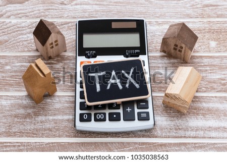 Tax sign on calculator with house model on wooden table
