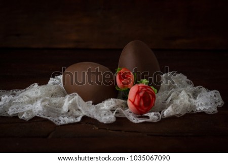 Chocolate Eggs, White Lace Tape, Artificial Decorative Roses on Dark Wooden Background. Easter concept.