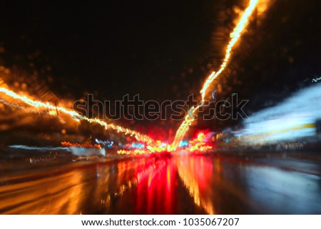 De focused image of rain falling on the road, looking out the window. Rain drops on window, rainy weather in the Montreal. Blurred car lights, long exposure photo of traffic. Wet asphalt.