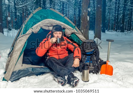 a lost tourist in the winter forest drinking tea while sitting in a tent