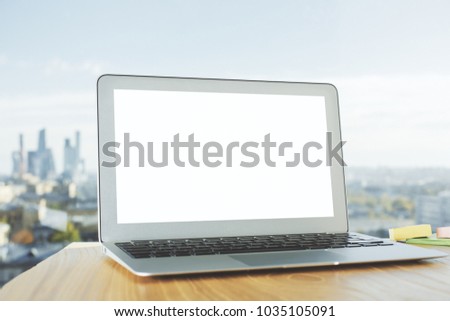 Close up of empty white laptop placed on wooden desk with blurry city view background. Advertisement concept. Mock up 