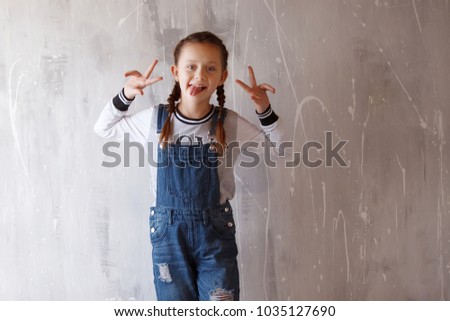 Young cute emotional teenager girl with braids in overalls portrait indoor. Crouching at the camera and smiling