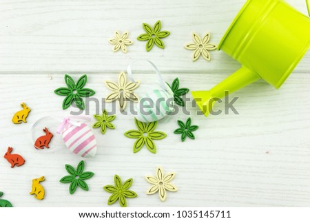 Easter abstract arrangement with pastel colored blue and pink eggs, artificial flowers and bunnies and green watering can on white patternend wooden background.