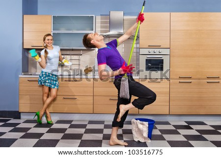 Modern kitchen - woman with sponge and smiling young man cleaning the floor at home and pretend to sing song with mop Royalty-Free Stock Photo #103516775