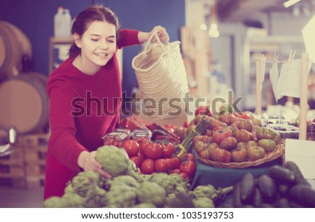 Young woman choosing artichokes in farm food store