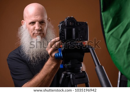 Studio shot of mature bald man with long gray beard against brown background