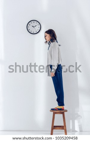 Attractive young girl standing on wooden chair under the clock