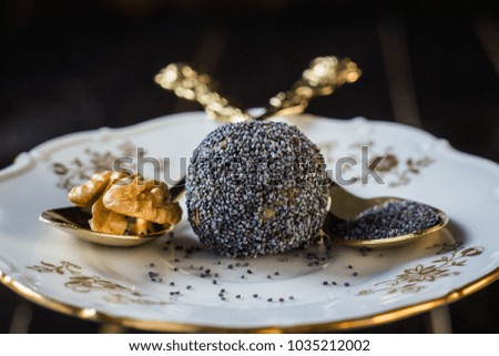 Candy with poppy seed and walnut on white and gold plate and gold spoons. Dark wooden background.