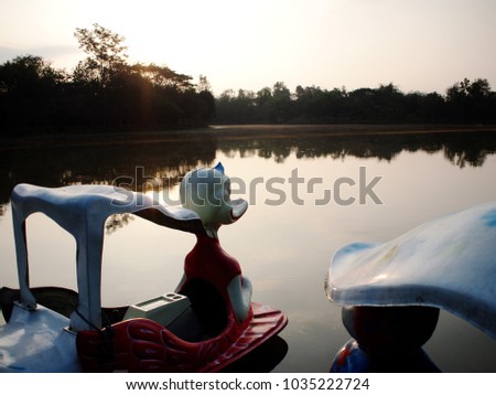 silhouette of colourful plastic paddle paddle boats evening time in a public park lake surrounding with tropical green tree on summer sunset bright golden yellow sky