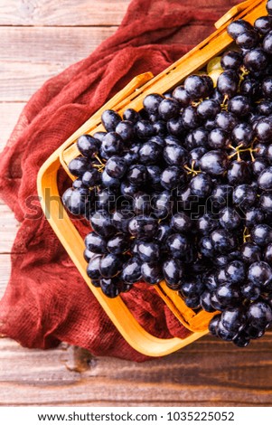 Photo from above of black grapes in wooden basket with claret cloth