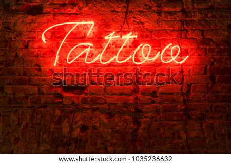 Glowing red neon signboard word tattoo on a brick dark background.