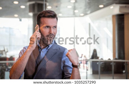 Successful businessman talking phone in modern interior, success sign