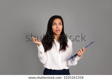 Young beautiful woman is thoughtfully holding a folder and pen on a gray background