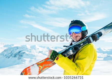 Picture of sports woman in helmet with skis on her shoulder against background of winter hills