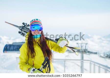 Sports woman in mask with skis on her shoulder on background of snowy hill, blue sky in winter
