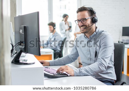 Smiling customer support operator with hands-free headset working in the office. Royalty-Free Stock Photo #1035280786