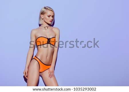 beautiful girl posing in orange bikini isolated on purple