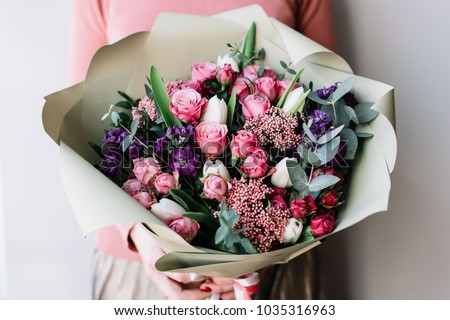 Very nice florist woman holding a beautiful colourful blossoming flowers bouquet of fresh roses, carnations, tulips, eucalyptus on the grey wall background Royalty-Free Stock Photo #1035316963