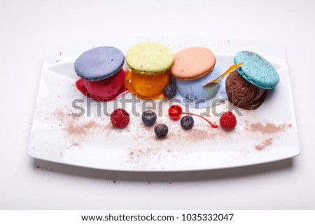 Rainbow colored ice cream and macaroons set on white plate with berries