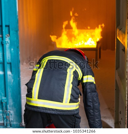 Fireman during training. Fire extinguisher. Golden yellow flames / fire in the background. Red helmet.