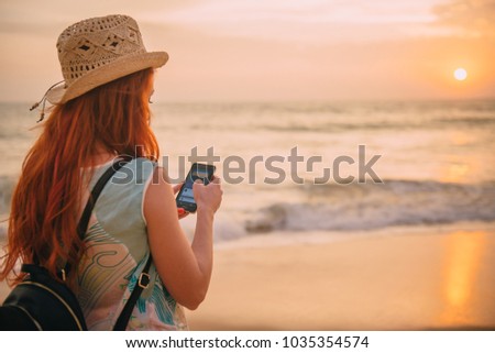 young woman tourist uses a smartphone on the ocean shore at sunset, rear view