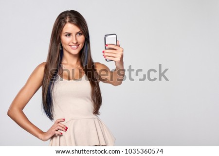Closeup of beautiful smiling brunette woman taking self portrait on smart phone, over grey background