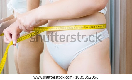 Closeup image of young woman in panties measuring her waist
