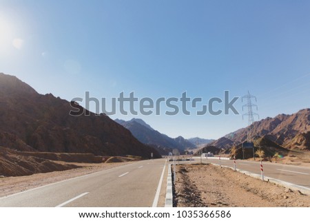 A two-lane highway to each side in the midst of a hot desert with many traffic signs on the move in a sunny day.