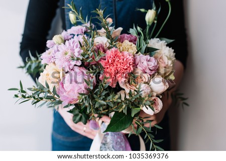 Very nice florist woman holding a beautiful colourful blossoming flower bouquet of peony, carnations, roses, eustoma, chrysanthemums, pistachio leaves on the grey wall background Royalty-Free Stock Photo #1035369376