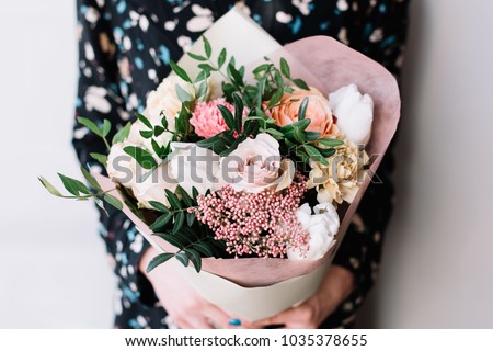 Very nice florist woman holding a beautiful colourful blossoming flower bouquet of fresh Quicksand roses, carnations, ranunculus, peony, pistachio leaves on the grey wall background Royalty-Free Stock Photo #1035378655
