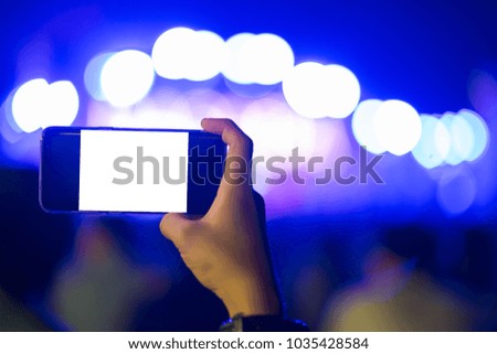 Hand holding smart phone with blank white screen. Photo shot blurry party and concert of event background and copy space. Technology and lifestyle. Smartphone white screen. 