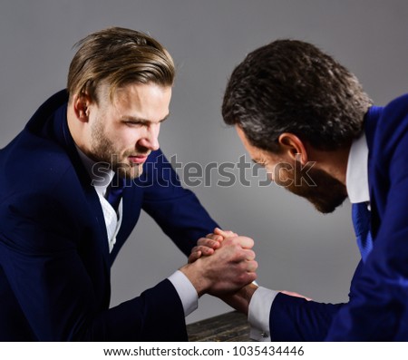 Confrontation of business leaders. Men in suit or businessmen with aggressive faces compete in armwrestling on table on dark background. Businessmen fighting for leadership. Business rivalry concept.