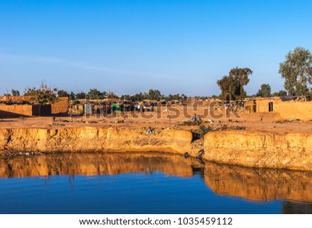 Eastern township of Ouagadougou on a sunny day with a hole filled with rainwater in the foreground, Burkina Faso. Royalty-Free Stock Photo #1035459112