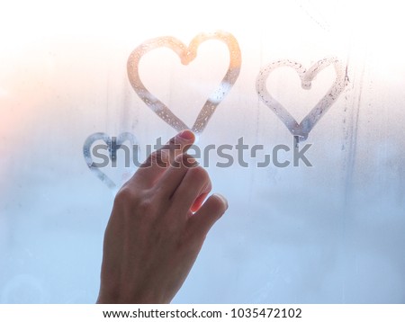 A beautiful female hand draws a heart on a misty window.