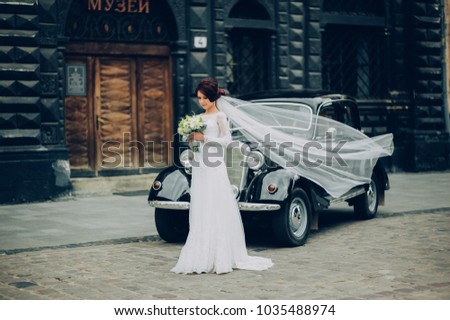Happy bride and groom hugging and posing near old retro car before wedding ceremony