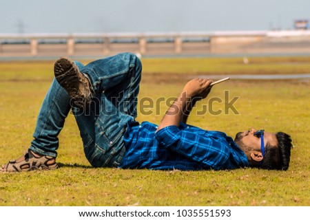 Picture of an Indian guy on the ground using his smartphone.