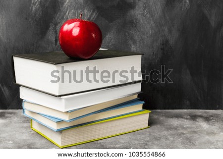 Pile of various books and red apple on dark background. Copy space