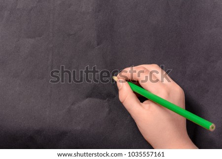 The hand of a little boy writes a pencil on a black background