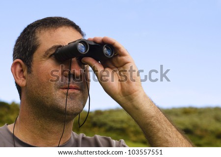 Adult man looking through binoculars outdoors.Concept photo of curious, spy,search,surveillance,spying,peeping, nosy man.Real people. Copy space