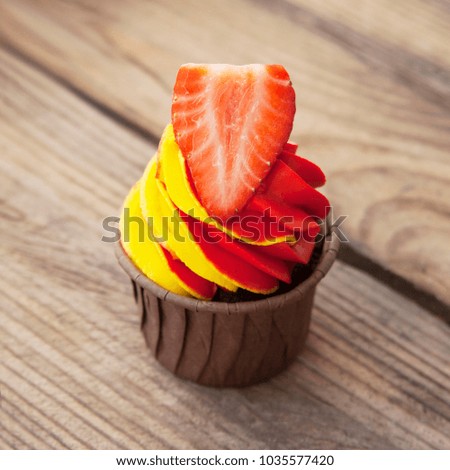Tasty chocolate cupcake with strawberry on a wooden table. Chocolate cupcake with whipped chocolate cream, decorated fresh strawberry. Picture for a menu or a confectione