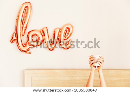 woman's hand with a cup of coffee in bed, the concept of the beginning of a new day, good morning. Love sign on the wall