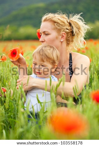 Pretty caucasian woman with her child in poppy field, focus on mother
