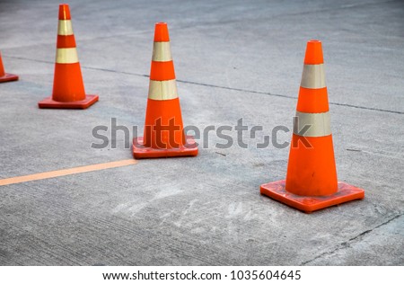 Three orange traffic cones on the concrete surface of the parking lot. 