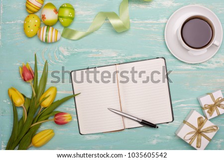 Colored easter eggs,  tulips, gift boxes and blank daily log with pen  and cup of coffe on a green wooden background. Top view with copy space.