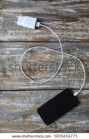 White charger and black smartphone on old wooden background. Information technology vertical digital photo. Modern layout on vintage texture.
