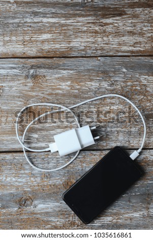 White charger and black smartphone on old wooden background. Information technology vertical digital photo. Modern layout on vintage texture.