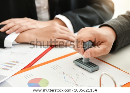Businessman hand is stamping on document while discussing at meeting.