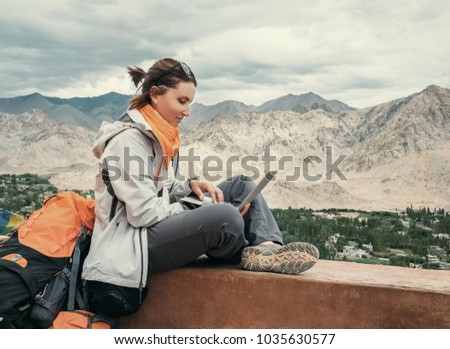 Backpacker with laptop sits on the top view point under mountain settelment